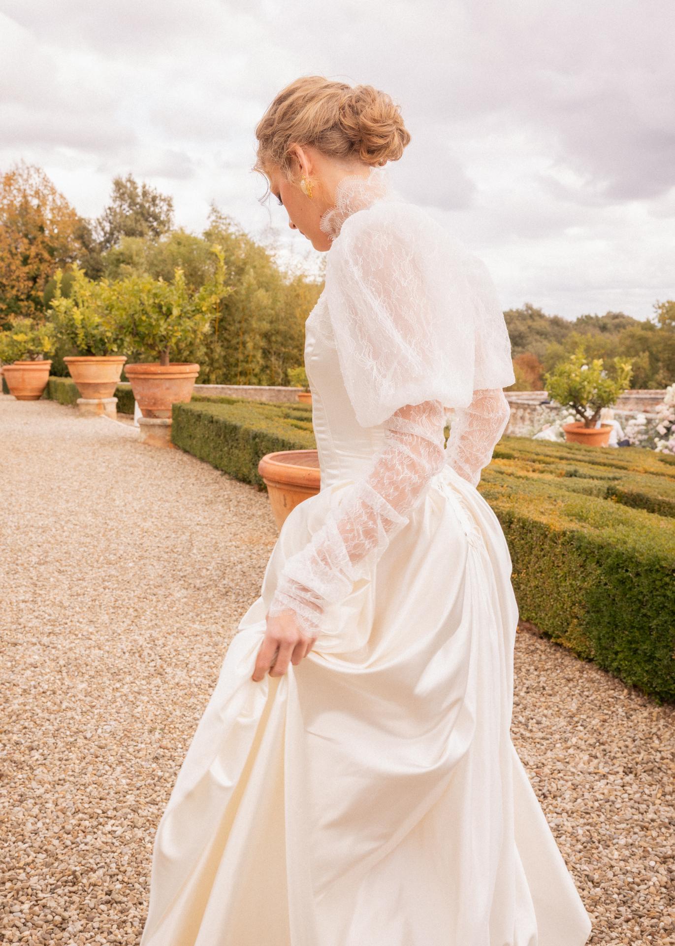 Bride in an elegant lace wedding dress standing in the gardens of Castello di Celsa, Tuscany, during a luxury destination wedding.
