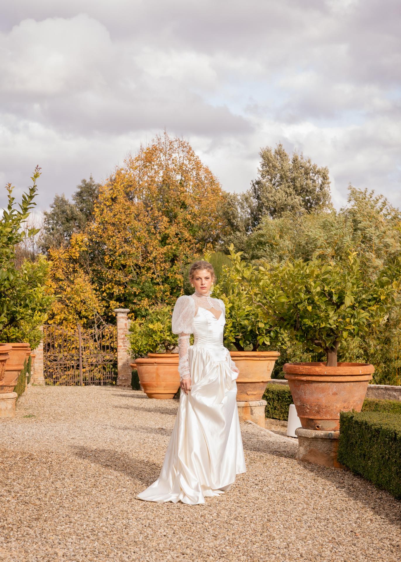 Bride in an elegant lace wedding dress standing in the gardens of Castello di Celsa, Tuscany, during a luxury destination wedding.