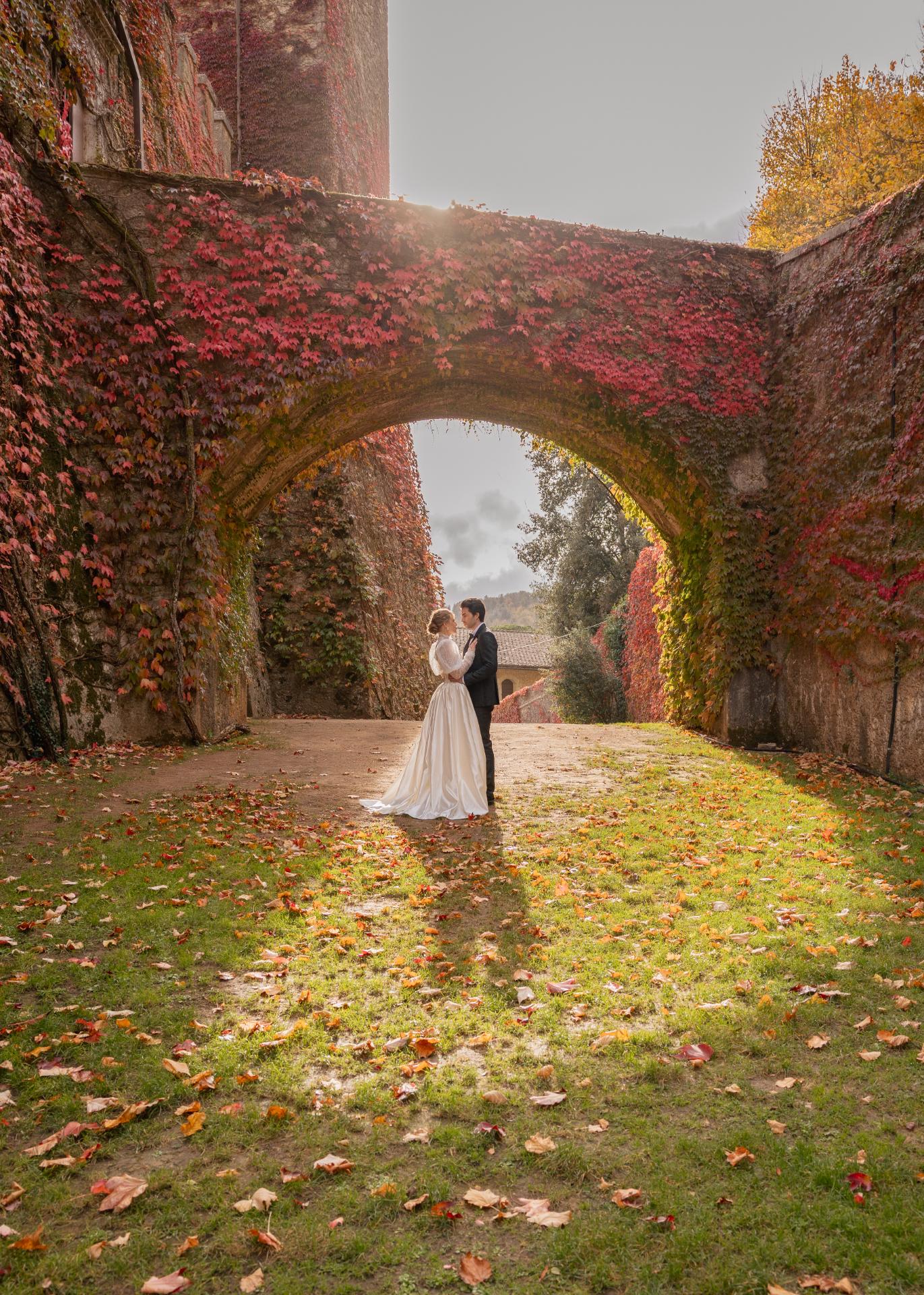 Bride and groom standing under an ivy-covered arch during an autumn wedding at Castello di Celsa in Tuscany.