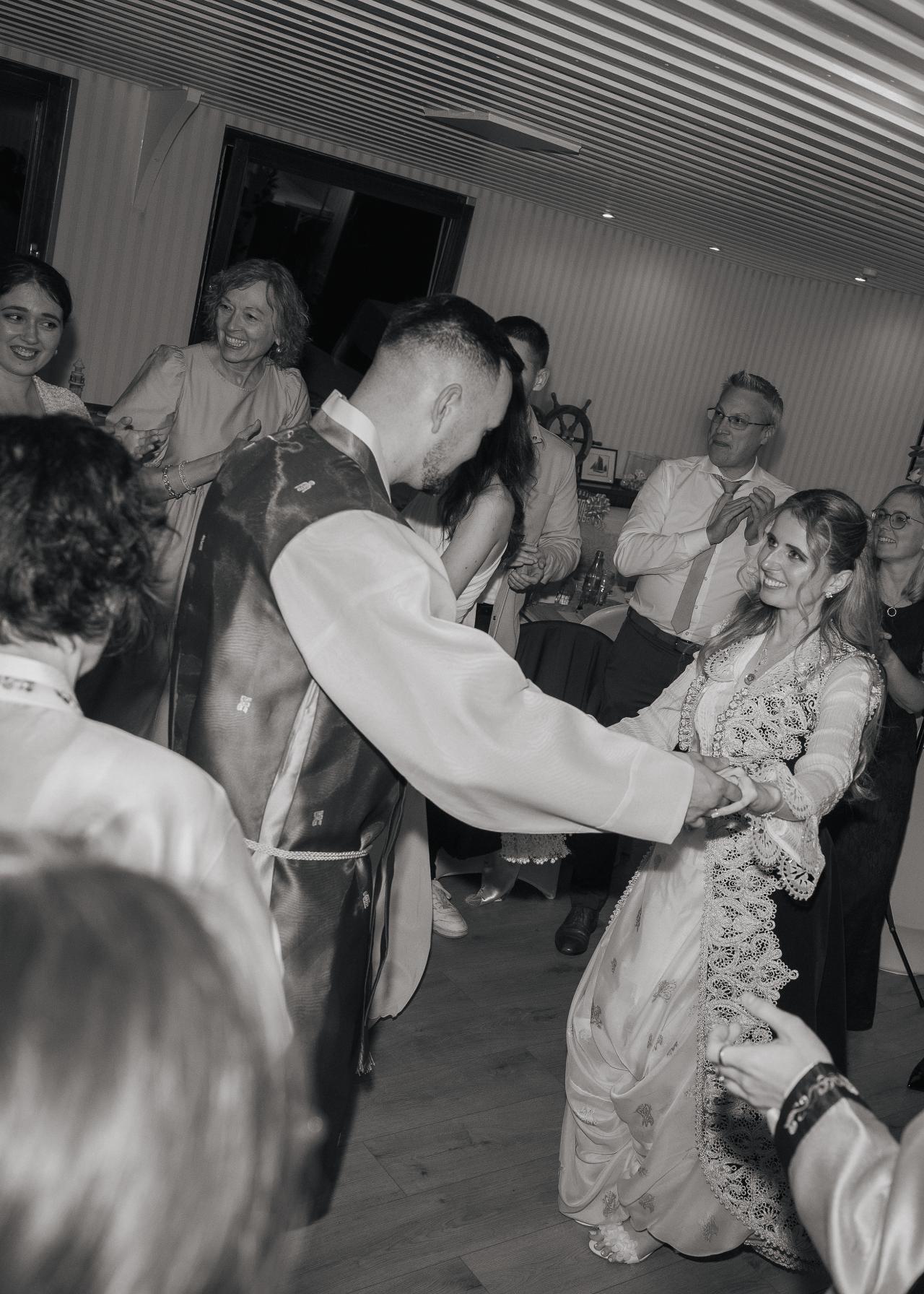 Bride and groom dancing together during a lively wedding reception, surrounded by cheering guests