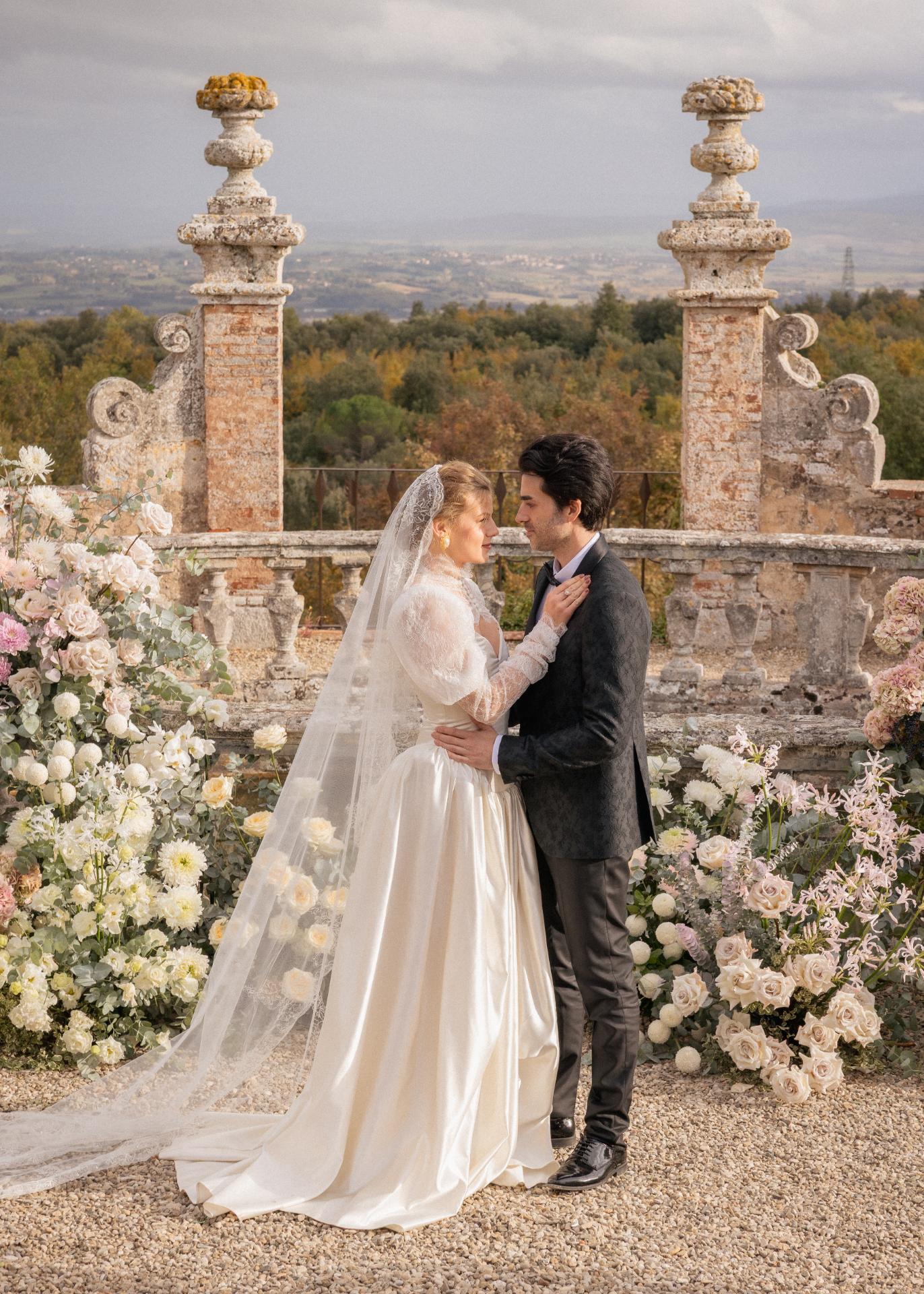 Romantic wedding portrait of bride and groom at Castello di Celsa in Tuscany, standing in front of an elegant floral ceremony backdrop