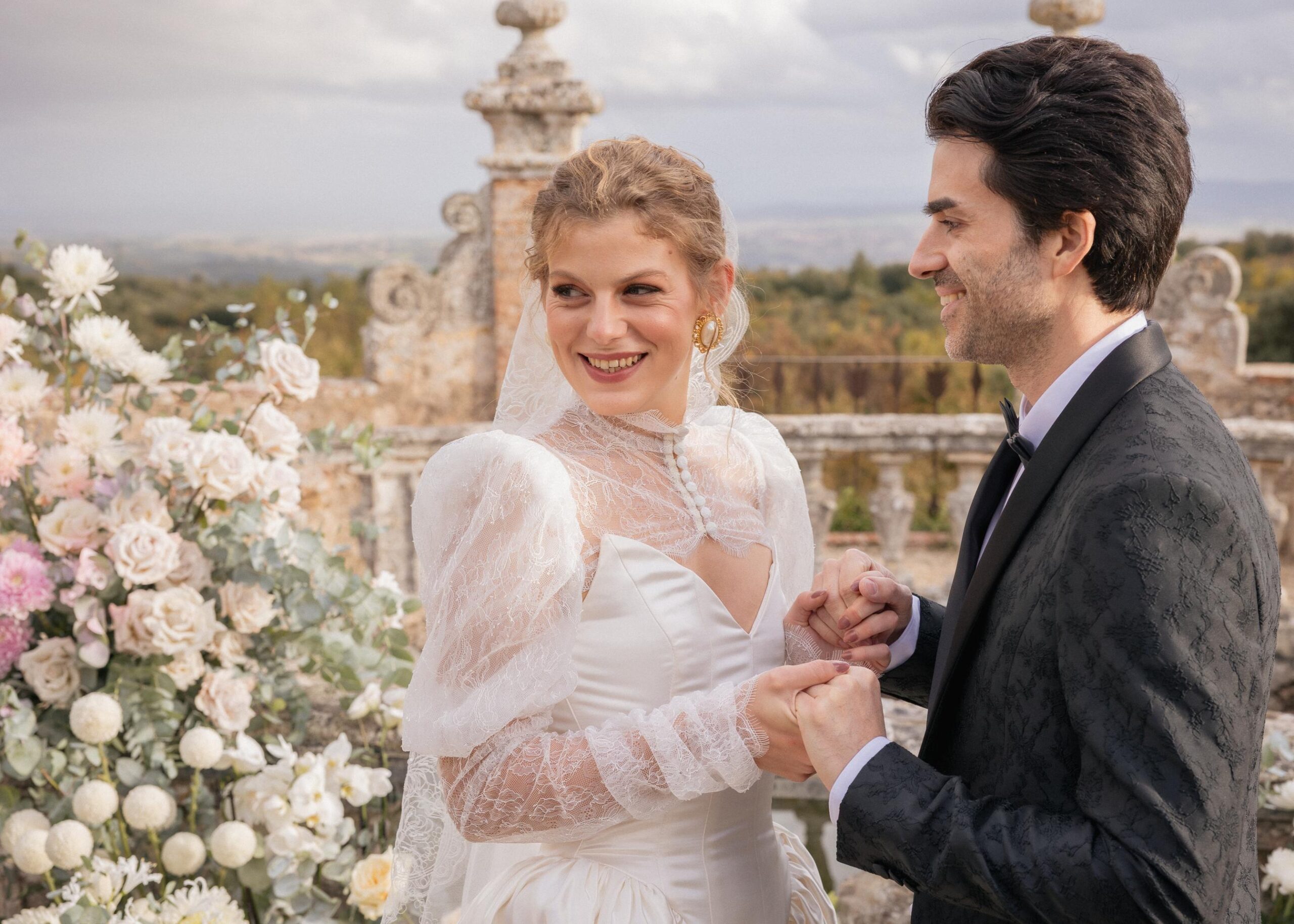 Bride and groom holding hands during an elegant wedding ceremony at Castello di Celsa, featuring a lace long-sleeve wedding dress and refined floral design