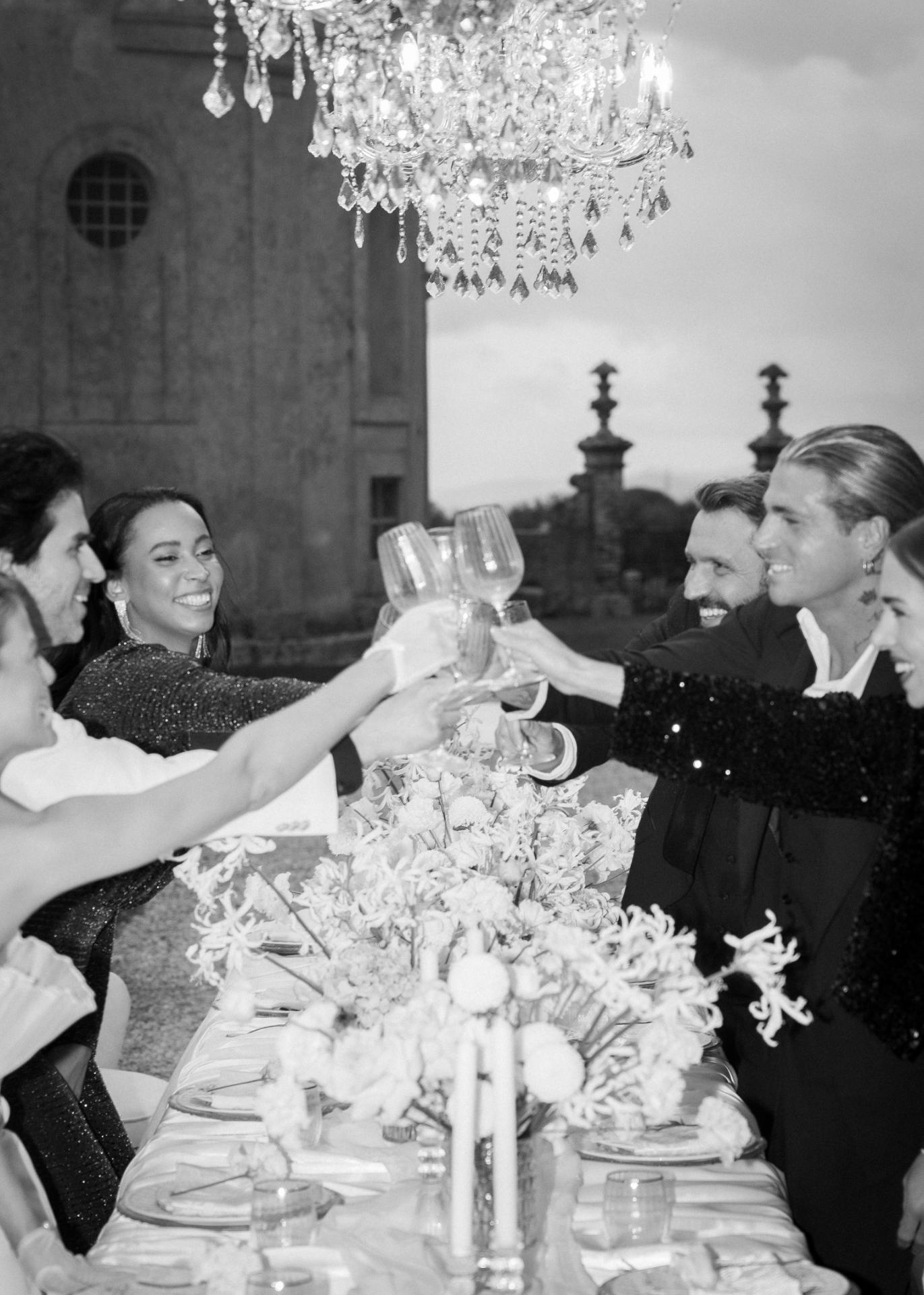 Wedding guests raising champagne glasses during an elegant outdoor wedding dinner under crystal chandeliers.