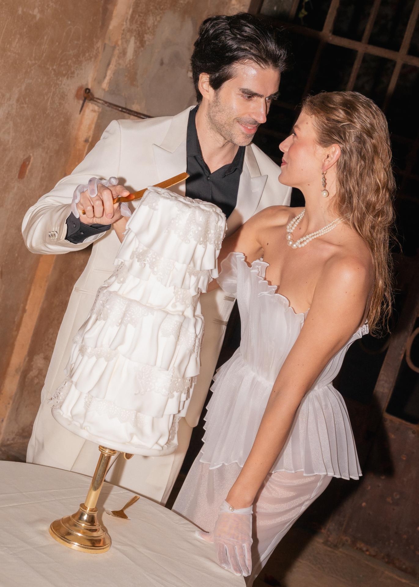Bride and groom cutting a modern white wedding cake during an elegant evening wedding celebration.