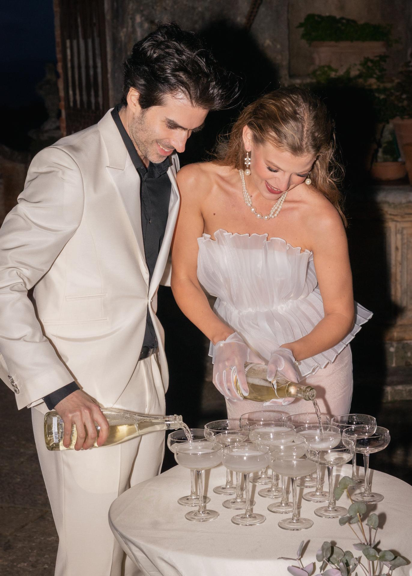 Bride and groom celebrating with champagne at a wedding reception table, captured in a dramatic editorial wedding photograph.