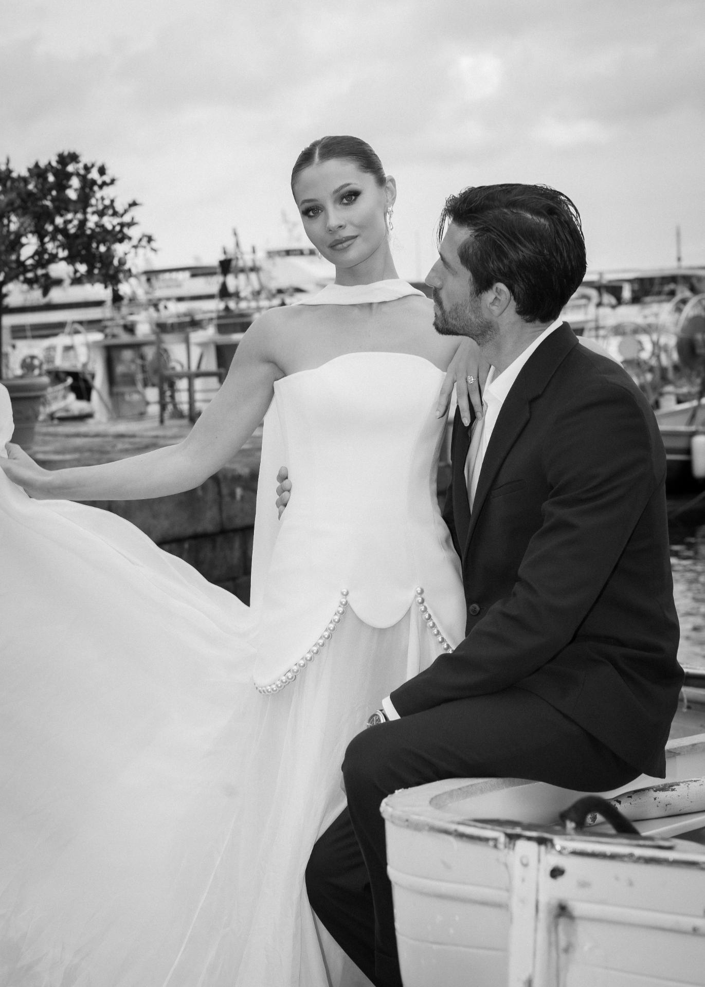 Stylish bride in a modern wedding dress and groom posing by an Italian harbor, capturing an elegant destination wedding moment.