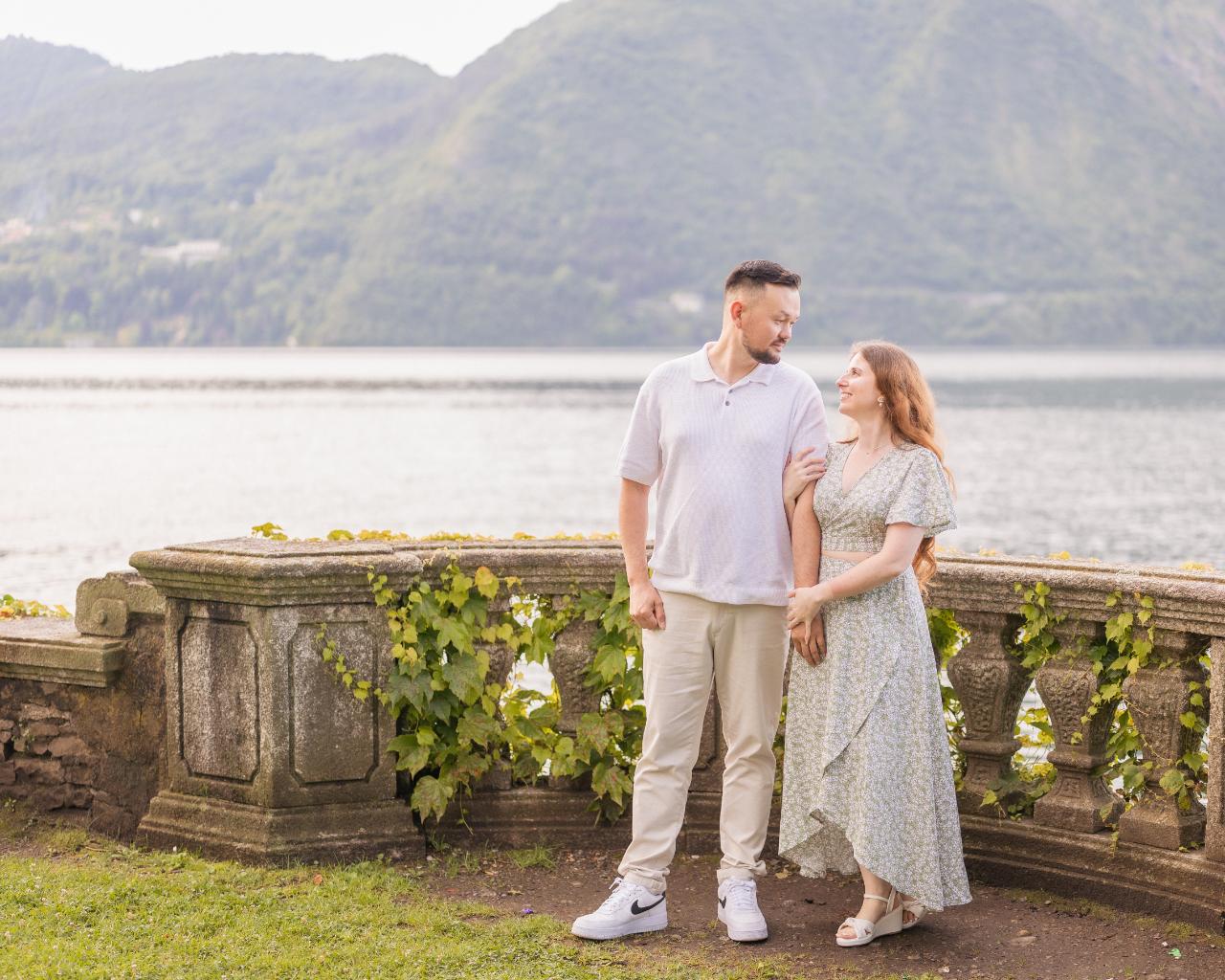 Engaged couple standing by a villa balustrade overlooking Lake Como
