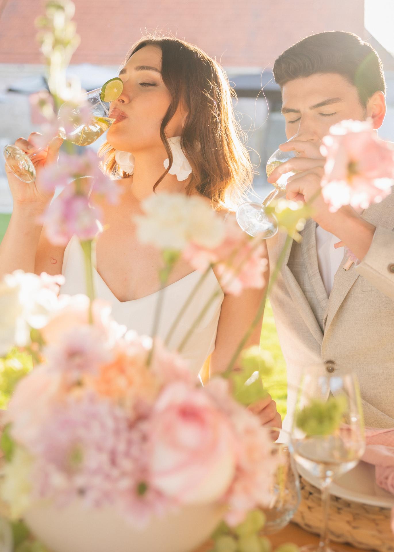Bride and groom enjoying a summer wedding cocktail hour, drinking refreshing drinks surrounded by pastel floral arrangements in golden light