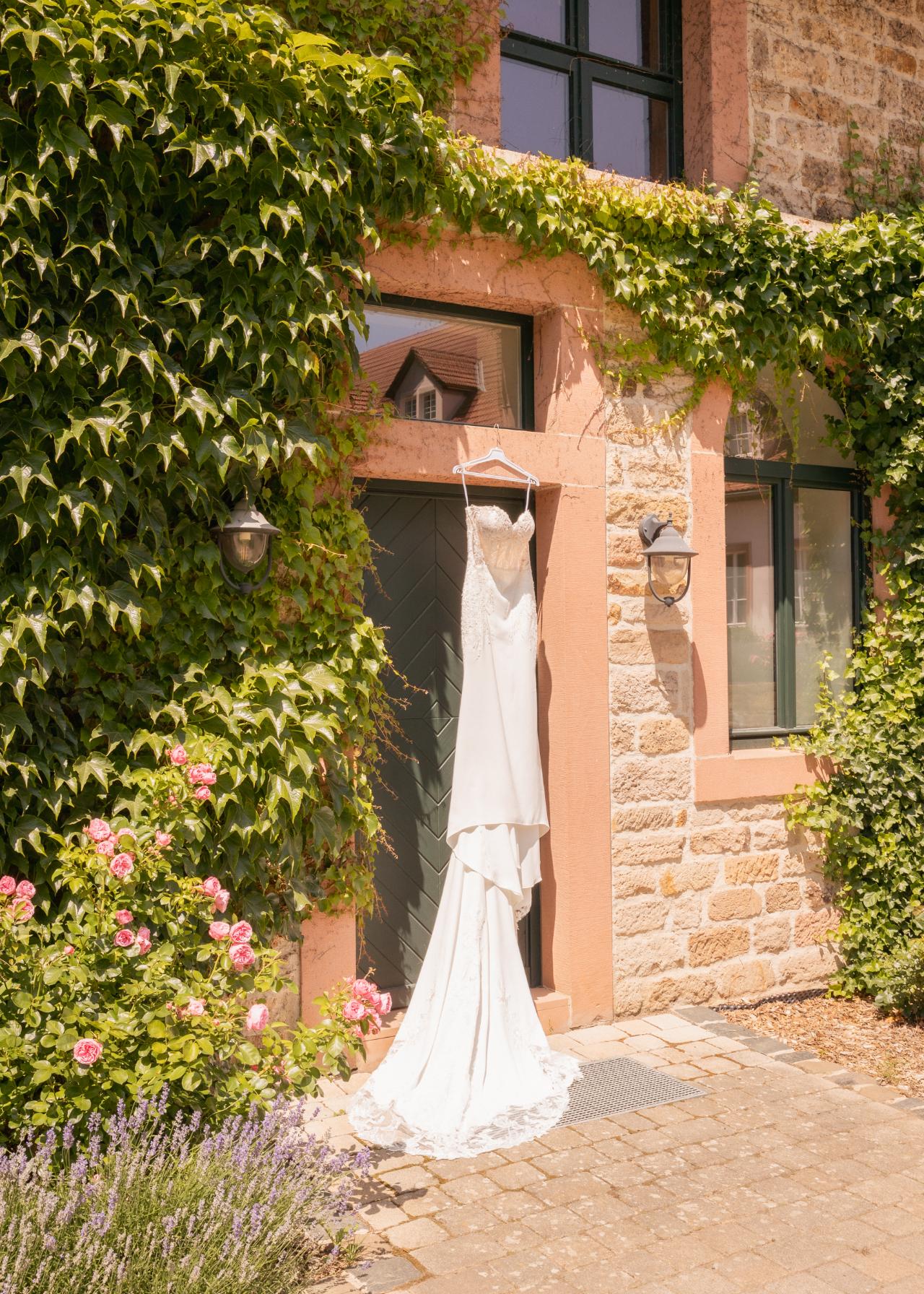 Elegant wedding dress hanging outside on a stone villa covered in ivy, natural light bridal getting ready detail