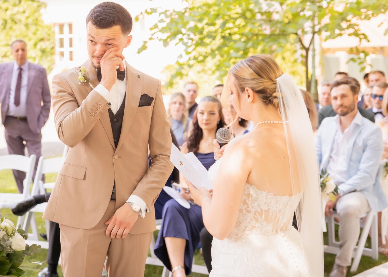 Emotional groom wiping away tears while listening to the bride’s wedding vows during an outdoor ceremony