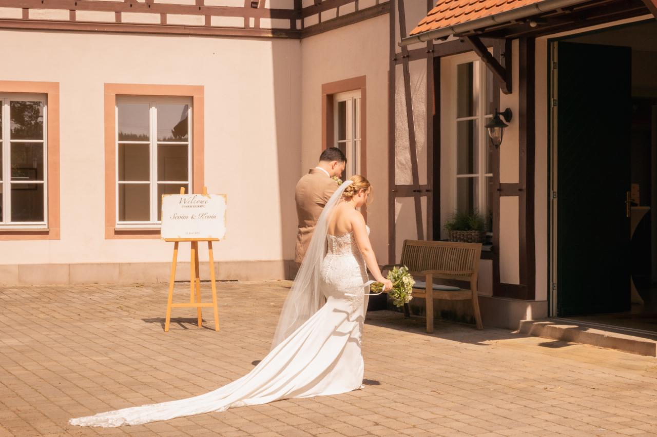 Bride and groom arriving at their wedding venue, bride with long veil and train walking through an elegant courtyard