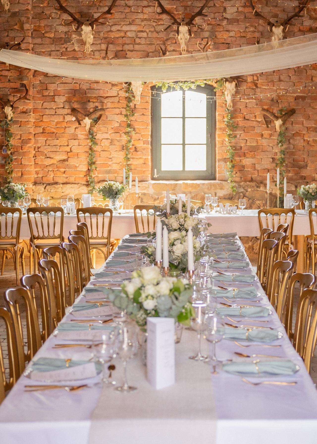 Elegant long table wedding reception with white florals, candles and refined table styling in a rustic brick barn