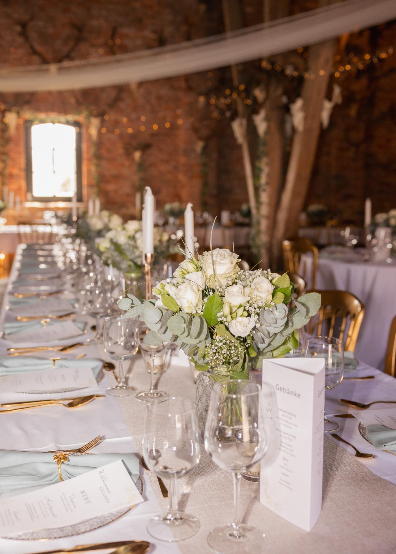 Elegant wedding table setting with white floral centerpiece, candles and refined tableware in a rustic barn reception