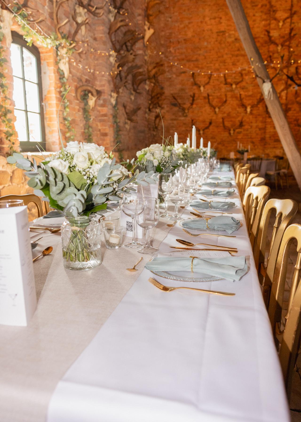 Elegant wedding table setting with white floral arrangements, gold cutlery and soft green napkins