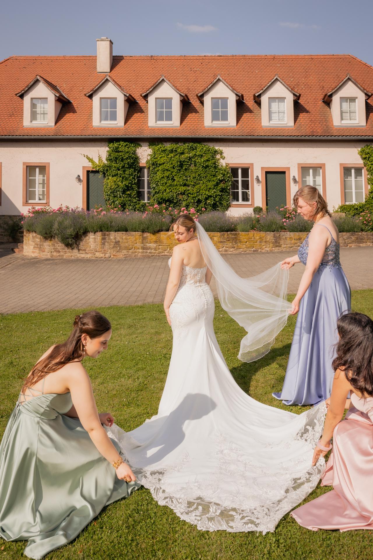 Brautjungfern helfen der Braut ihre Hochzeitskleid zu richten und ihren Kathedralschleier