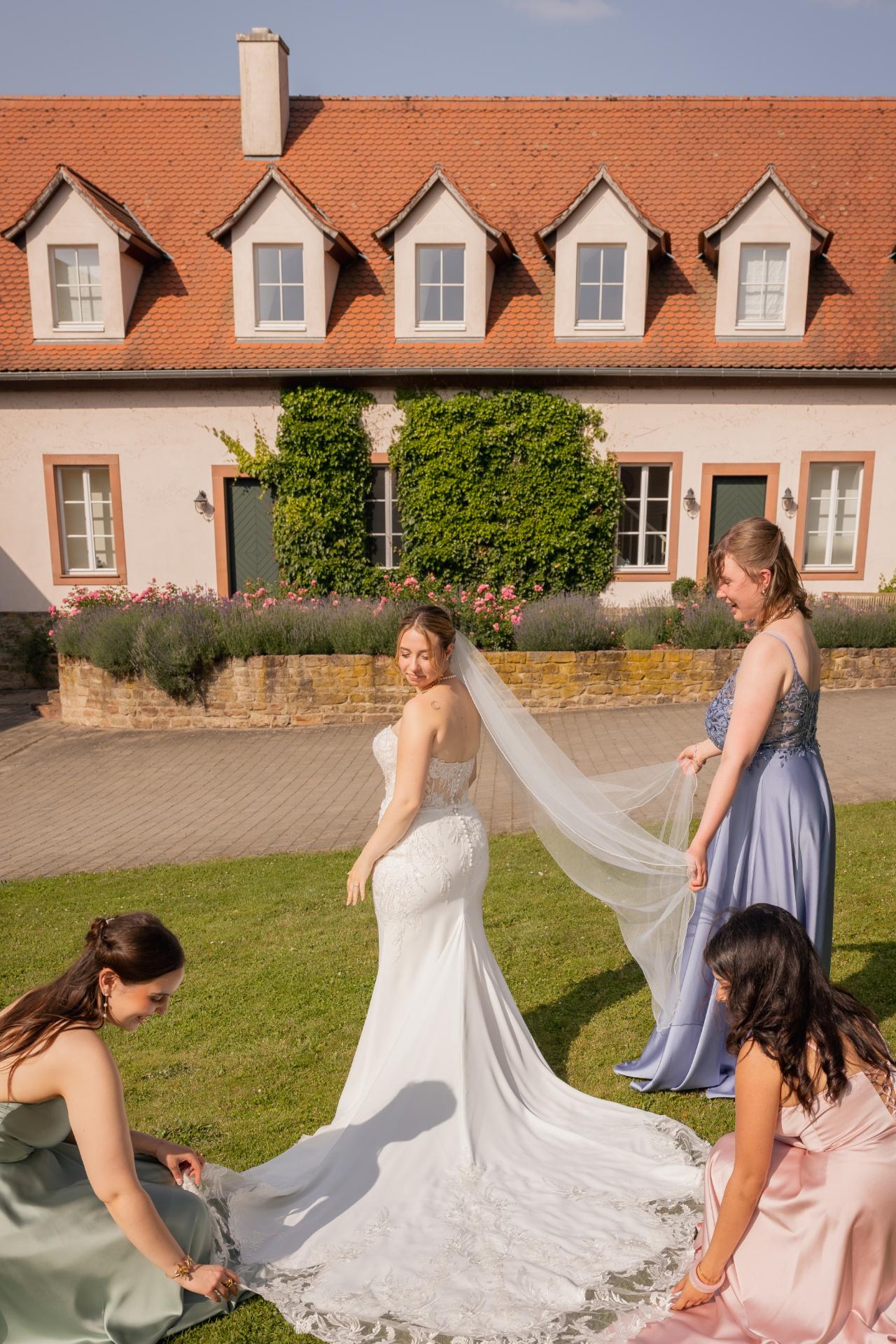 Bride with bridesmaids adjusting her wedding dress train and veil in the garden of an elegant estate