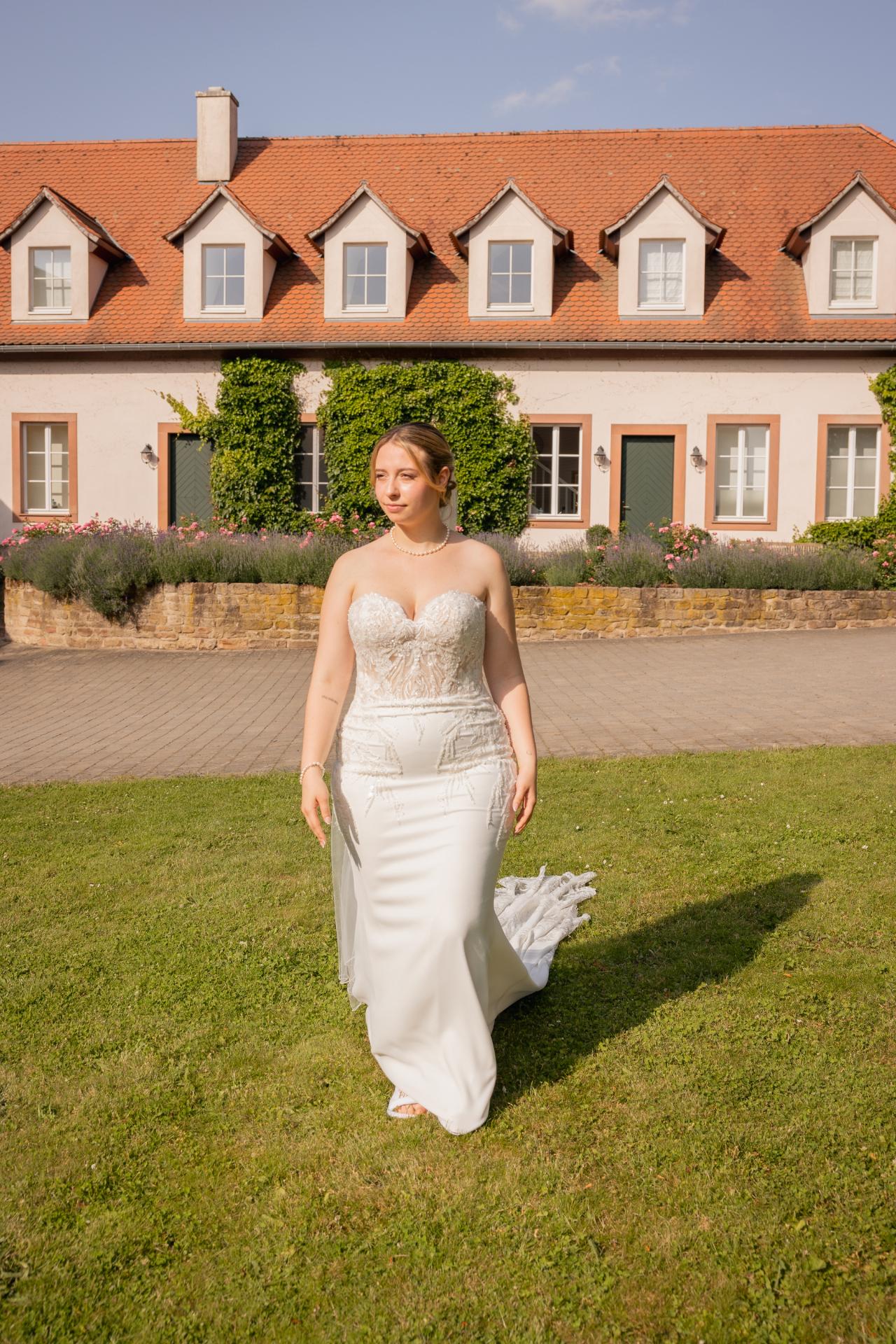 Bride walking through a garden in a modern lace wedding dress in front of an elegant estate