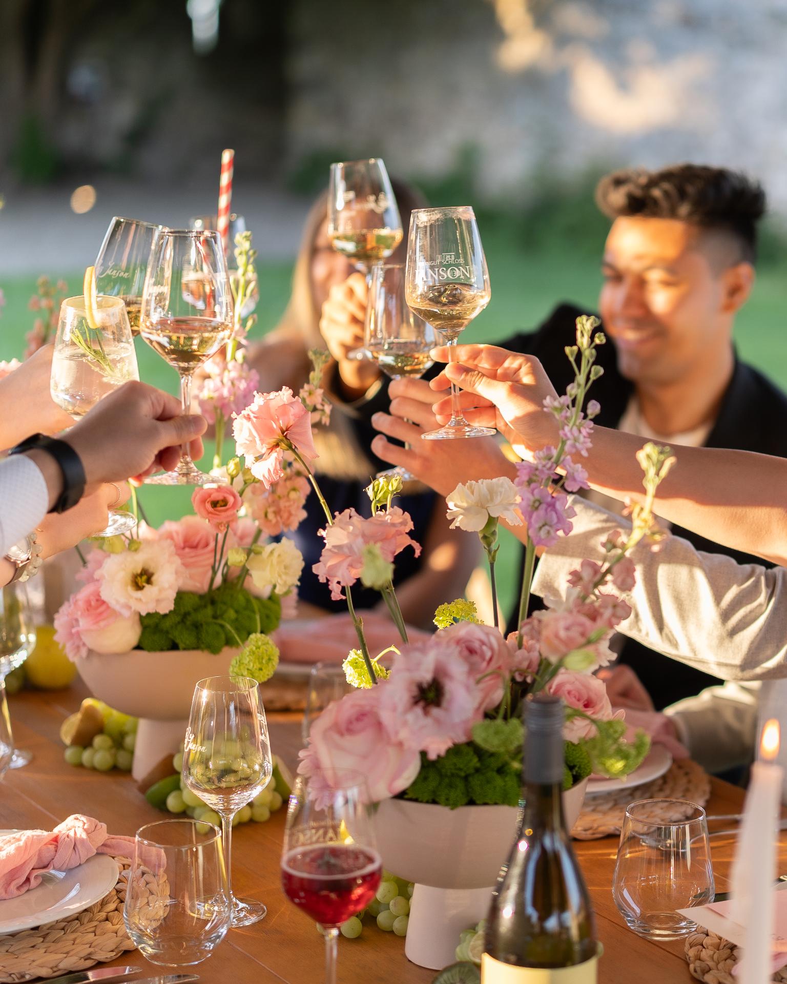Wedding guests clinking wine glasses during an outdoor reception with floral table decor