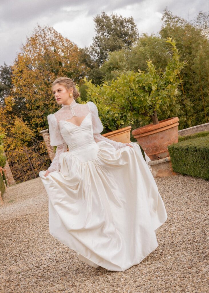 Bride in an elegant lace wedding dress standing in the gardens of Castello di Celsa, Tuscany, during a luxury destination wedding.