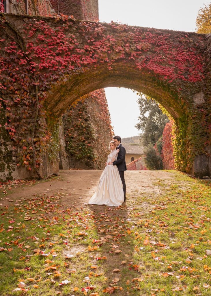 Bride and groom standing under an ivy-covered arch during an autumn wedding at Castello di Celsa in Tuscany.