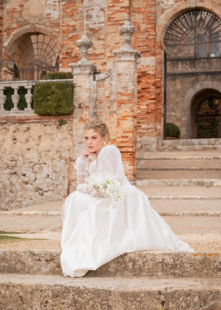 Bride in a classic lace wedding dress seated on stone steps at Castello di Celsa, Tuscany, for a luxury Italian wedding.