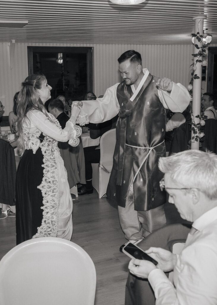 Bride and groom dancing together in traditional cultural wedding attire during an energetic reception, surrounded by guests
