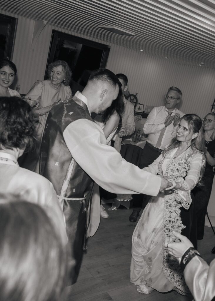 Bride and groom dancing together during a lively wedding reception, surrounded by cheering guests