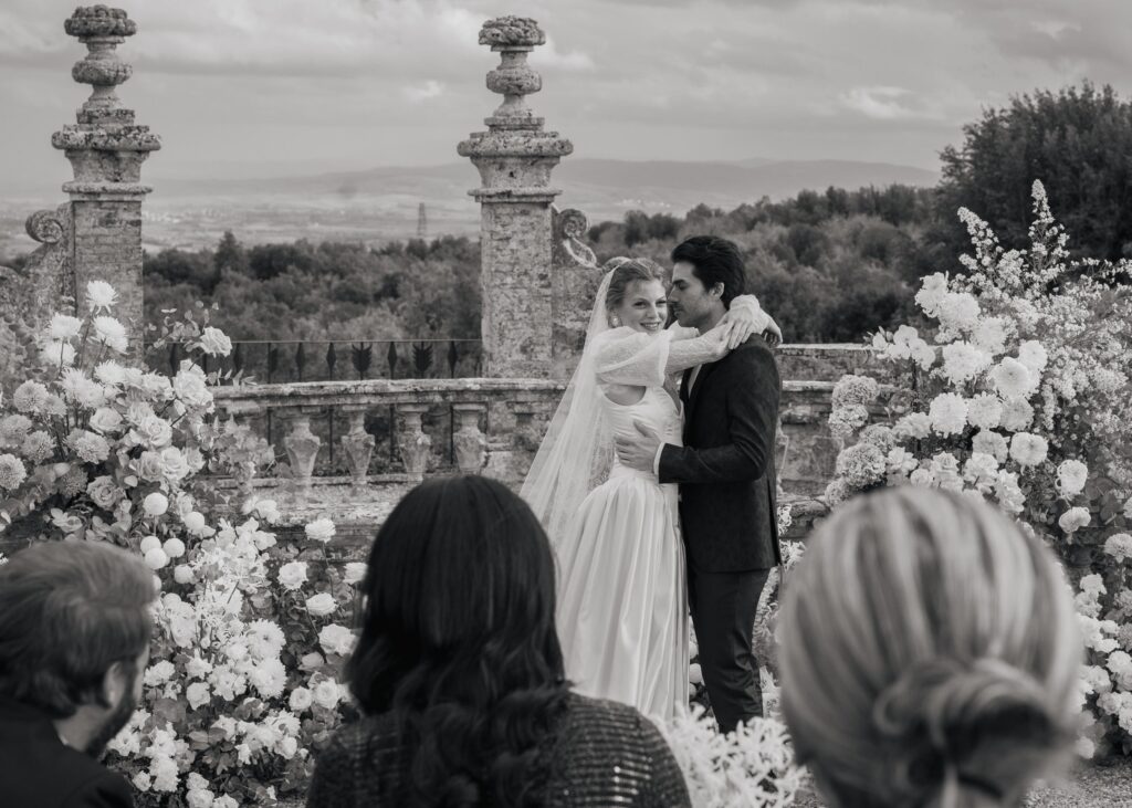 Black and white wedding ceremony at Castello di Celsa with bride and groom embracing in front of an elegant floral altar in Tuscany
