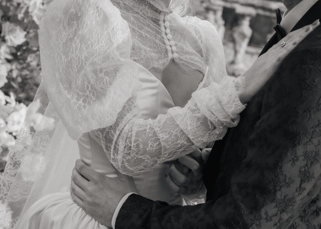 Black and white close-up of a bride and groom embracing at Castello di Celsa, highlighting lace wedding dress sleeves and elegant tailoring