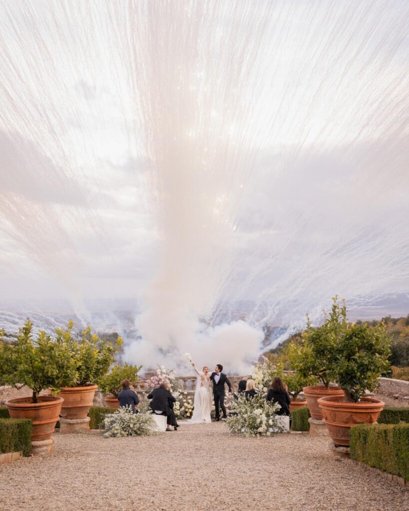 Bride and groom celebrating their wedding ceremony at an Italian villa with dramatic fireworks and floral aisle décor overlooking the countryside.