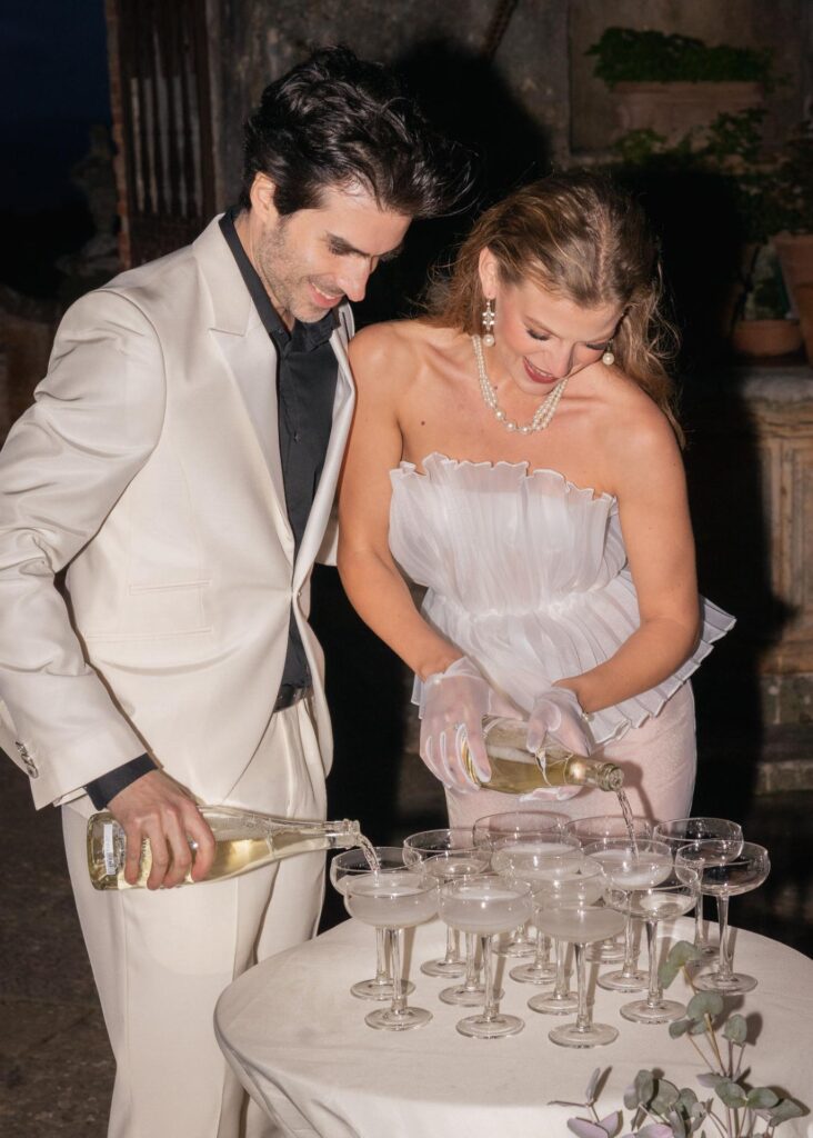 Bride and groom celebrating with champagne at a wedding reception table, captured in a dramatic editorial wedding photograph.