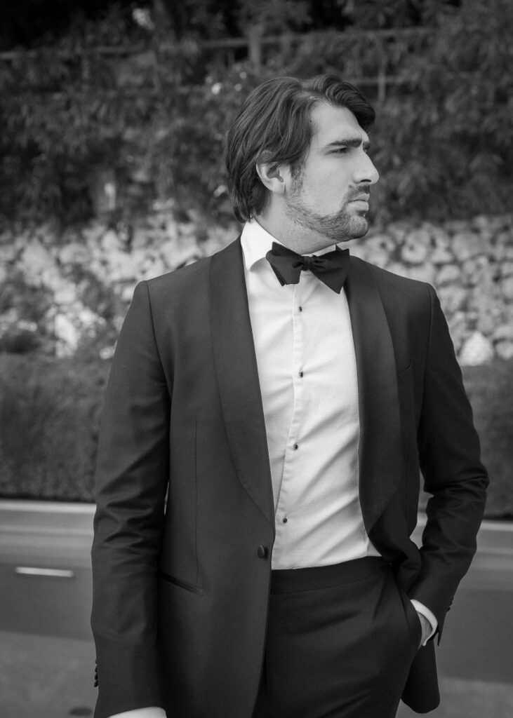 Black and white portrait of a groom in a classic tuxedo with bow tie, captured at a luxury wedding with an elegant, editorial style.