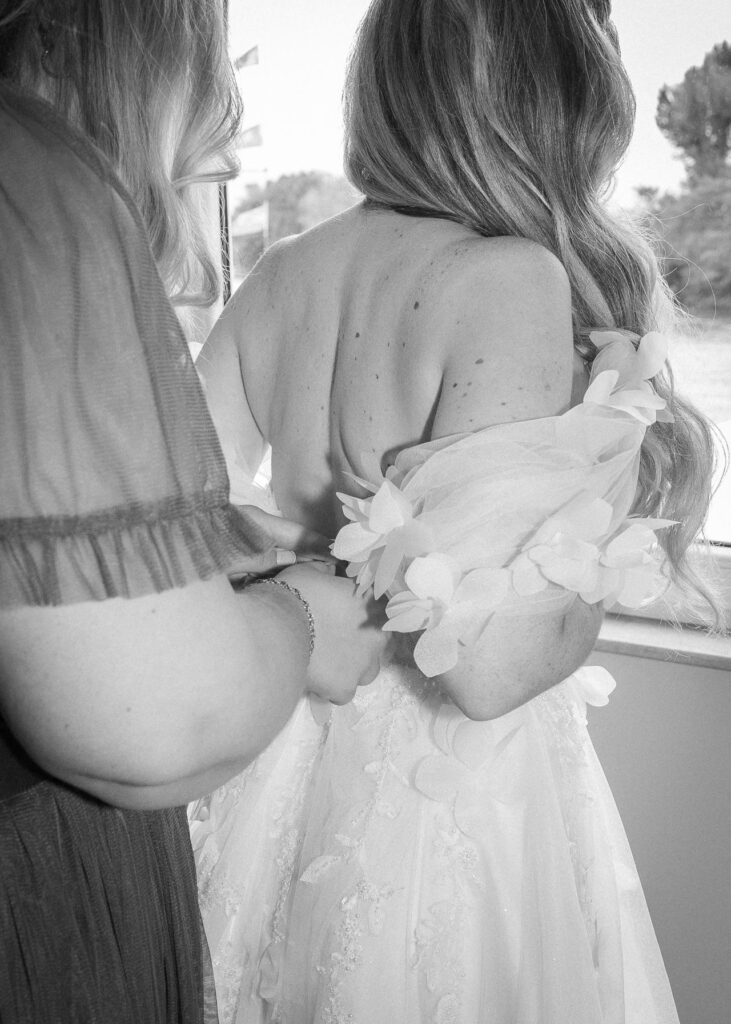 Bride getting ready as her wedding dress is fastened from the back