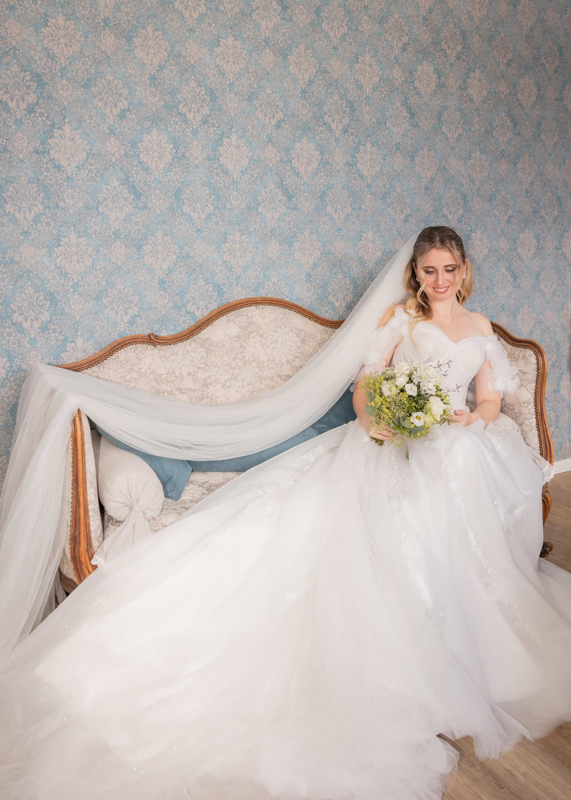 Bride seated on a vintage sofa with a long veil and bouquet