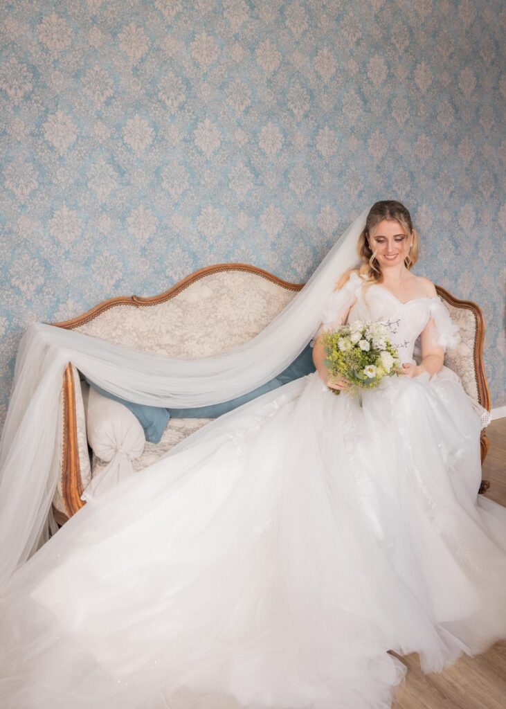 Bride seated on a vintage sofa with a long veil and bouquet