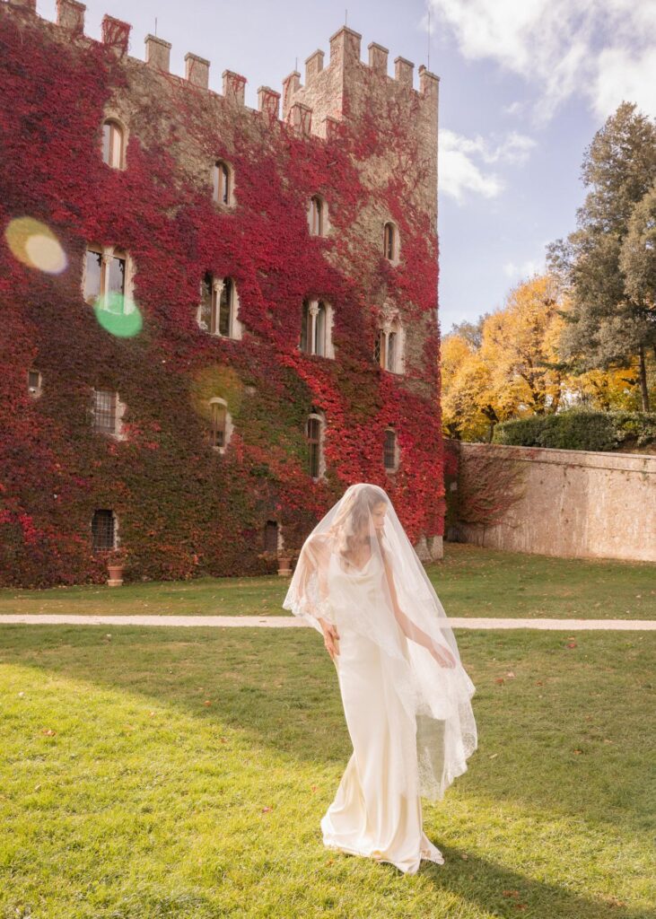 Modern bride in a minimalist silk wedding dress with pearl necklace at Castello di Celsa, Tuscany, captured in soft autumn light.