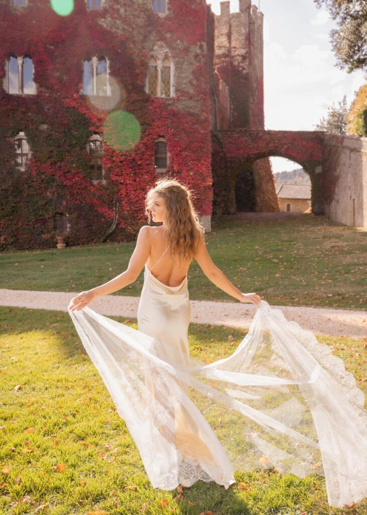 Modern bride in a minimalist silk wedding dress with pearl necklace at Castello di Celsa, Tuscany, captured in soft autumn light.