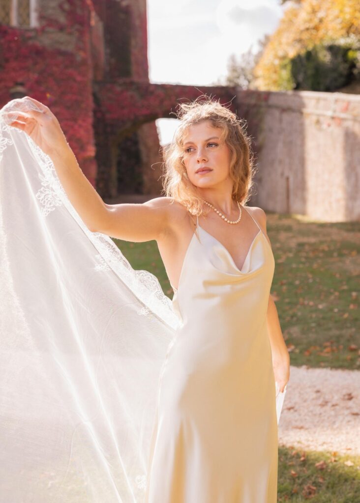 Modern bride in a minimalist silk wedding dress with pearl necklace at Castello di Celsa, Tuscany, captured in soft autumn light.