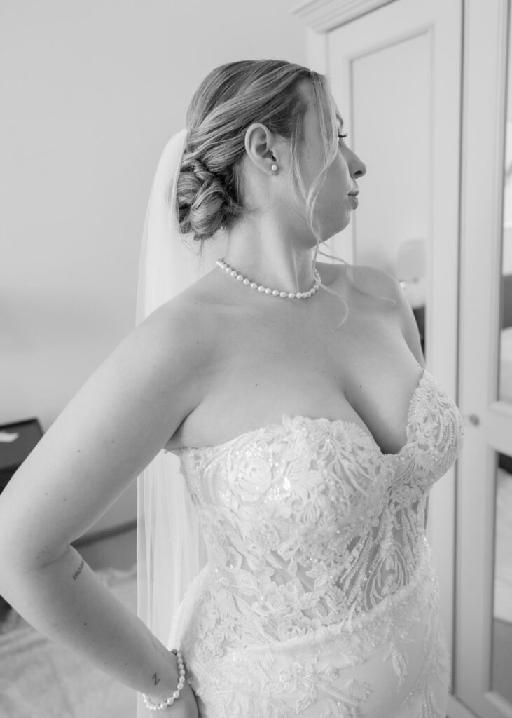 Bride getting ready in a strapless lace wedding dress, wearing a pearl necklace and veil during bridal preparations in black and white