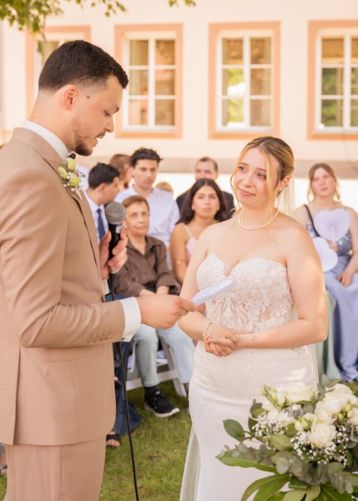 Groom reading his wedding vows to the bride during an emotional outdoor wedding ceremony surrounded by guests