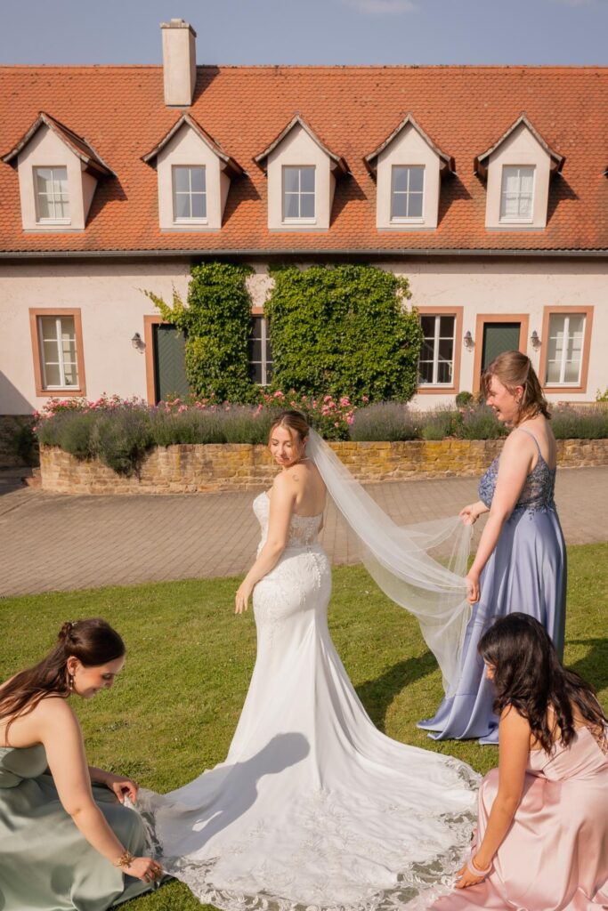 Bride with bridesmaids adjusting her wedding dress train and veil in the garden of an elegant estate