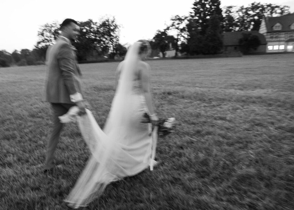 Bride and groom walking together across a field after the wedding ceremony, black and white fine art wedding photography capturing an intimate and emotional moment